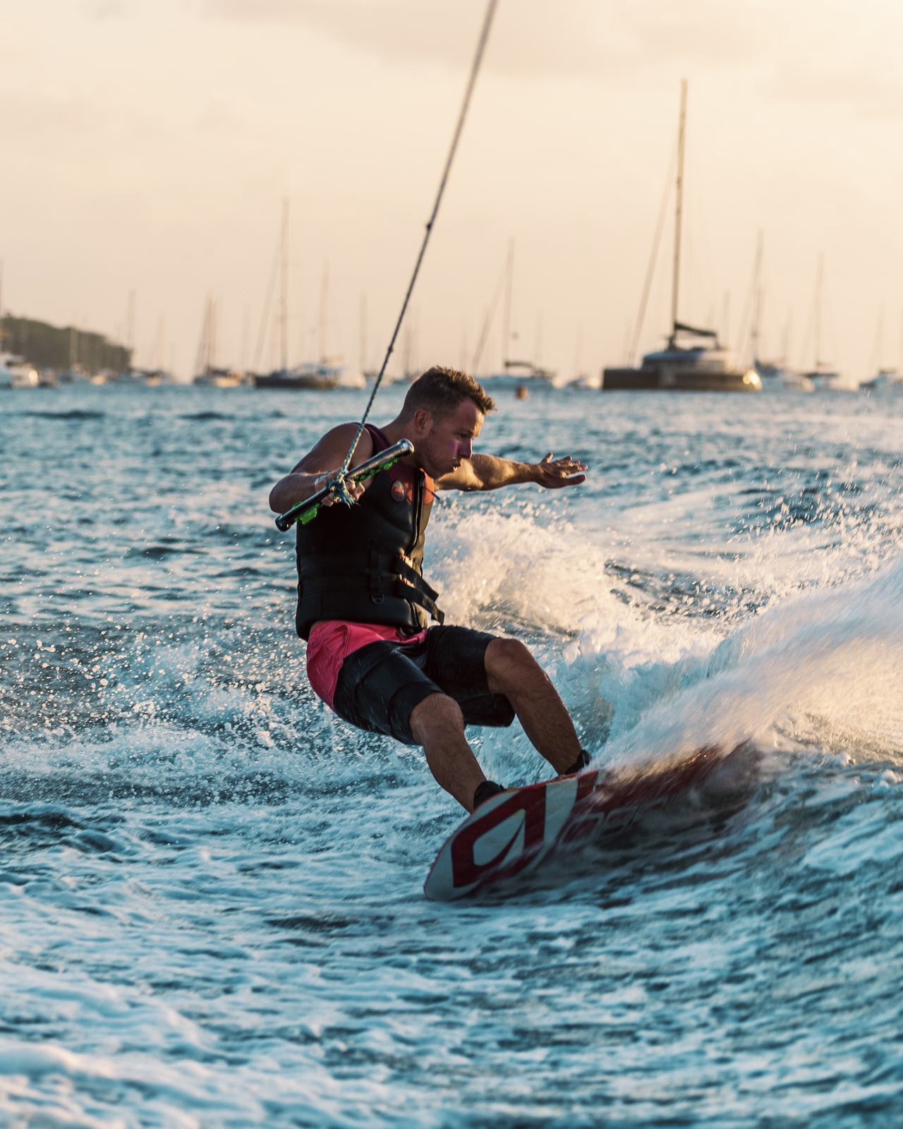 Wakeboarder carving through the water with sailboats behind him in Saint-Barthélemy