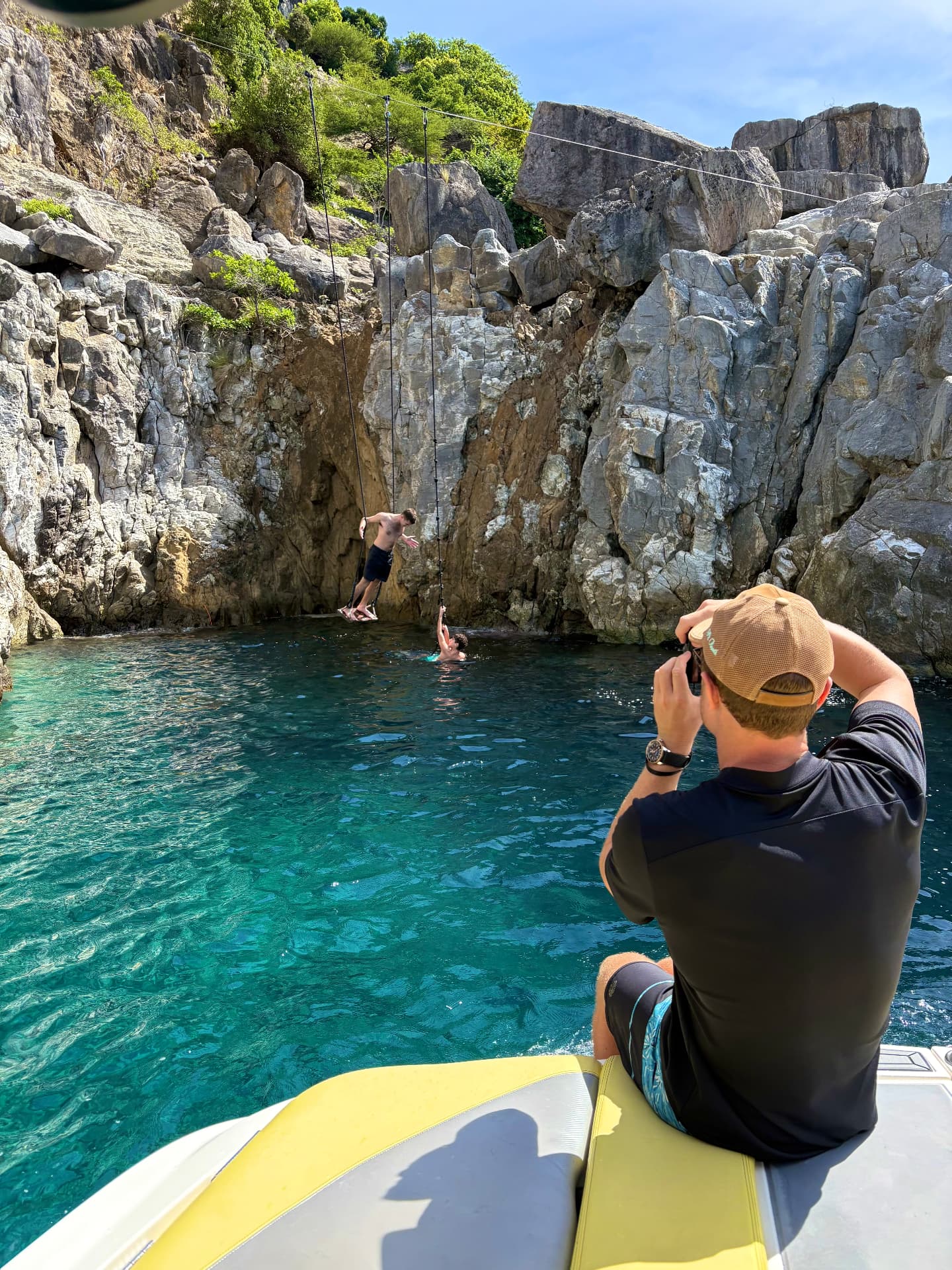 A person jumping from a rope swing over a rocky cove in Saint-Barthélemy